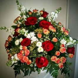 Large bouquet of red and peach roses in a white pedestal vase
