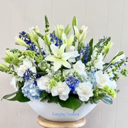 White lilies and roses arranged in a white bowl with blue accents
