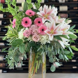 Pink gerberas and lilies in a clear glass vase with greenery