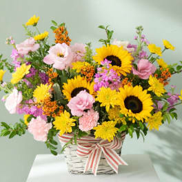Basket arrangement with sunflowers, pink blooms, and a striped ribbon