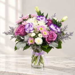 Bouquet of pink and purple flowers in a clear glass vase with a ribbon