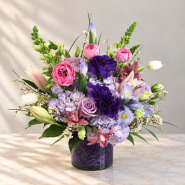Mixed bouquet of pink, purple, and white flowers in a dark glass vase