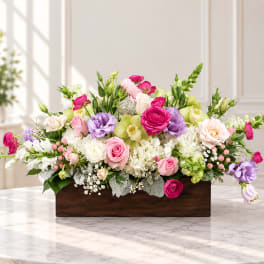 Mixed pink, purple, and white flowers arranged in a wooden box