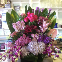 Large mixed floral arrangement with pink, purple, and white blooms in a black container