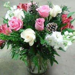 Pink and white roses arranged in a glass vase with greenery and a pinecone