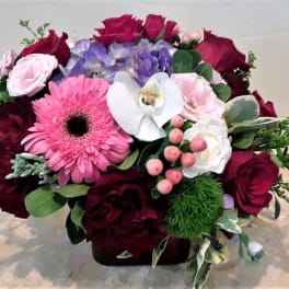 Mixed bouquet with roses, gerbera daisy, orchid, and hydrangea in a low container