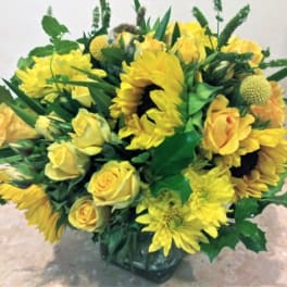 Yellow roses and sunflowers arranged in a glass vase