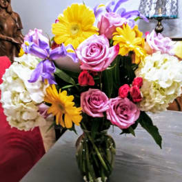 Bouquet of pink roses, yellow daisies, and white hydrangeas in a glass vase