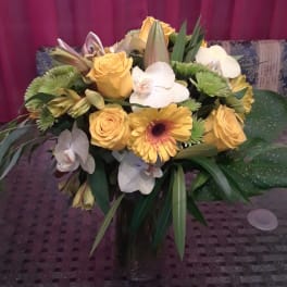 Bouquet of yellow roses, white orchids, and green chrysanthemums in a glass vase