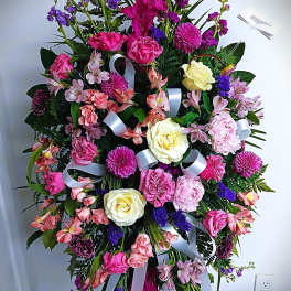 Large standing floral spray with pink, purple, and cream flowers and white ribbons