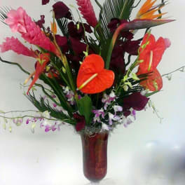 Tropical flower arrangement in a tall glass vase with orange anthuriums and pink blooms