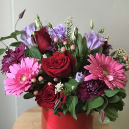 Bouquet of red roses, pink gerberas, and purple blooms in a red container