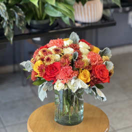 Mixed bouquet of red, yellow, white, and peach flowers in a glass vase