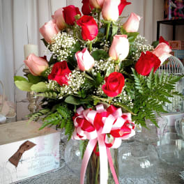 Red and pink roses in a glass vase with a ribbon bow