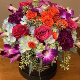 Round bouquet of pink, orange, and purple flowers in a black box