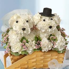 Two white floral dog figures in a basket, one with a veil and one with a top hat