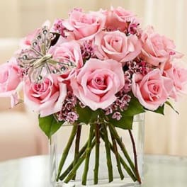 Pink roses arranged in a clear glass vase with a decorative butterfly pick