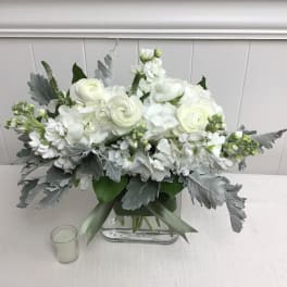 White floral arrangement in a clear rectangular vase with silver foliage