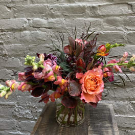 Bright mixed bouquet with coral roses and pink snapdragons in a glass vase