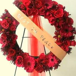 Red floral wreath with a peach ribbon on a stand