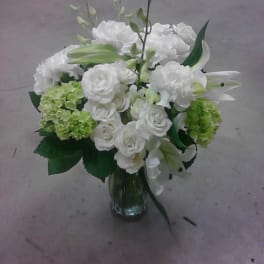 White floral arrangement in a glass vase with green accents