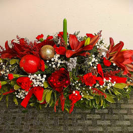 Low floral centerpiece with red lilies, roses, ornaments, and a green taper candle