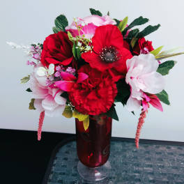 Red and pink floral arrangement in a red glass vase