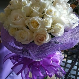 Bouquet of white roses wrapped in purple mesh with a ribbon