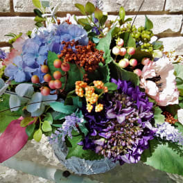 Colorful floral arrangement with blue, purple, and pink blooms in a low container