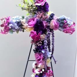 Cross-shaped floral arrangement in purple, pink, and white on a stand