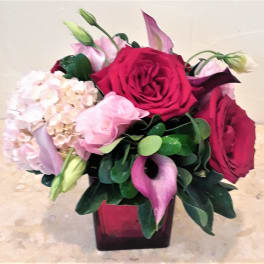 Bouquet of red roses, pink hydrangea, and calla lilies in a square vase