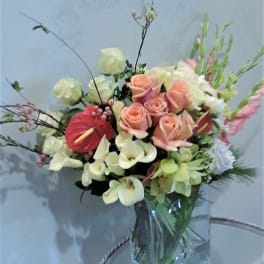 Mixed bouquet of peach roses, white calla lilies, and pink anthurium in a glass vase