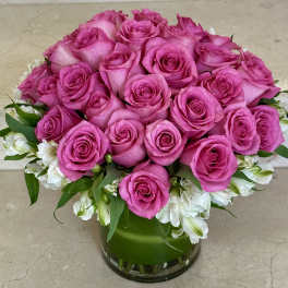 Pink roses arranged in a clear glass vase with white flowers around the base