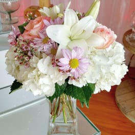 Bouquet of white hydrangeas, pink roses, and lilies in a clear glass vase