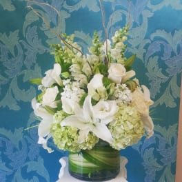 White floral arrangement in a glass vase with lilies, roses, and hydrangeas