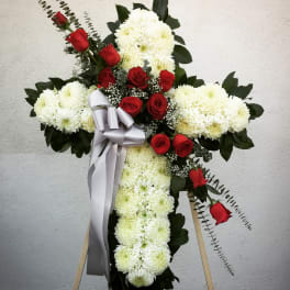 Cross-shaped floral tribute with white chrysanthemums and red roses, tied with a silver ribbon