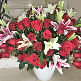 Large arrangement of red roses with white and pink lilies in a white ceramic vase