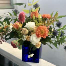Asymmetrical bouquet of orange dahlias and cream roses in a cobalt blue glass cube vase