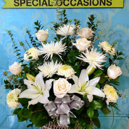 White floral arrangement in a woven basket with a silver ribbon