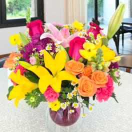 Colorful mixed bouquet in a glass vase with lilies, roses, and daisies