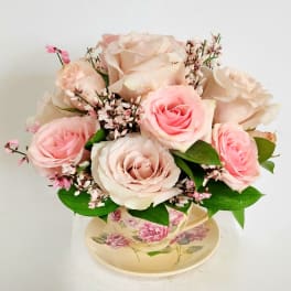 Pink and blush roses arranged in a floral teacup with a saucer