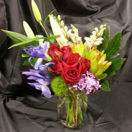Bouquet of red roses, lilies, and purple flowers in a glass vase