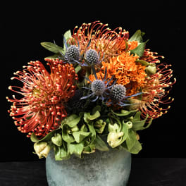 Orange and blue floral arrangement in a frosted glass vase