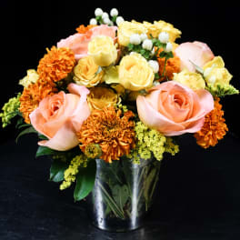 Pink and yellow roses with orange carnations in a glass vase