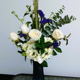 White roses and hydrangeas in a tall blue vase with purple accents