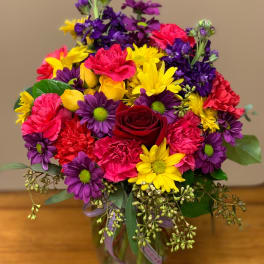 Colorful bouquet of daisies, carnations, and a red rose in a glass vase
