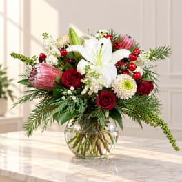 Red roses and white lilies in a glass vase with berries and greenery