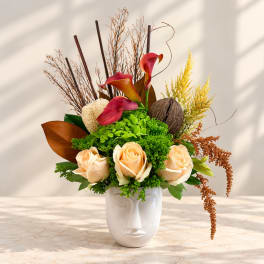 Arrangement of peach roses and red calla lilies in a white face vase