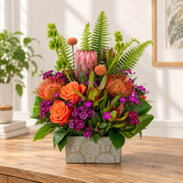 Tropical floral arrangement with orange roses in a patterned rectangular vase