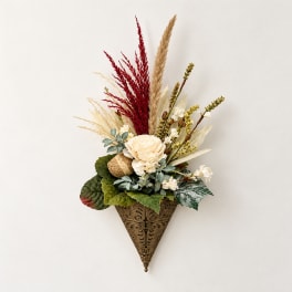 Wall-mounted floral arrangement with cream blooms and red dried grasses in a decorative cone holder